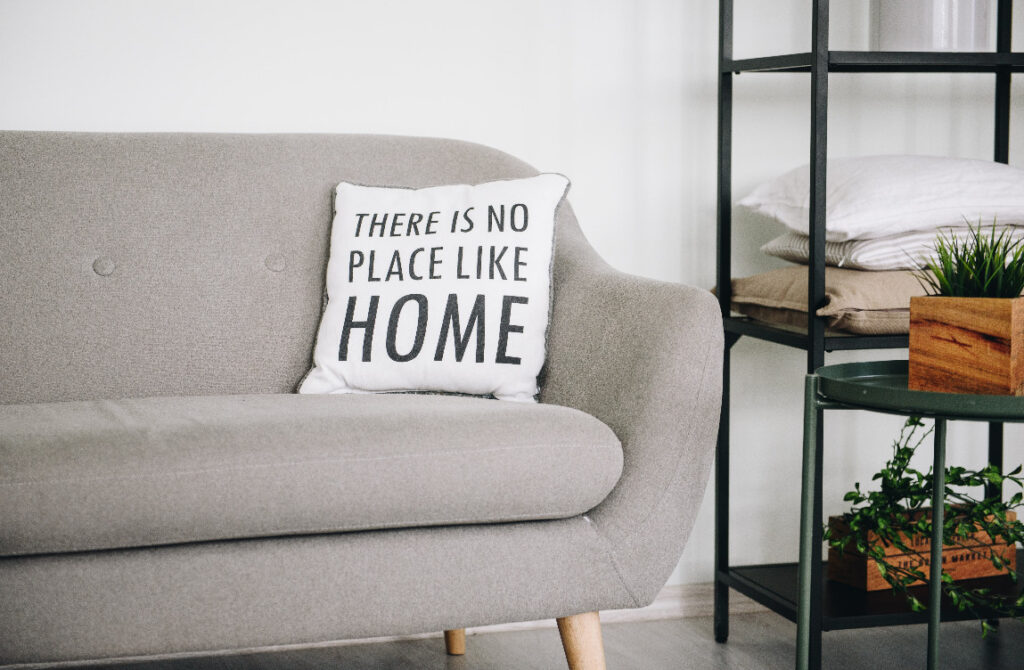 Comfortable couch with pillow that reads, "There is no place like home."